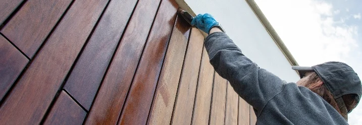 Person streicht Holzfassade mit Pinsel